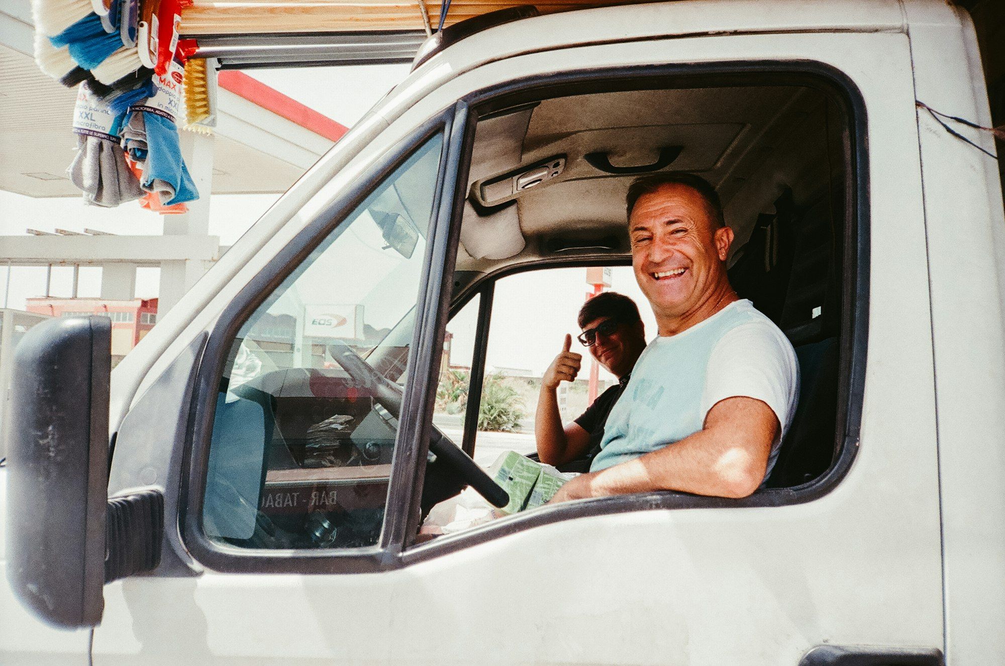 Conductor sonriente al volante de una furgoneta blanca con su compañero haciendo un gesto de aprobación