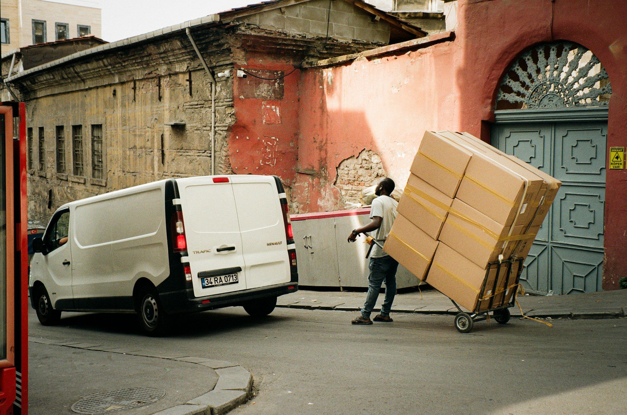 White van parked on an old-town street while a worker moves boxes with a hand truck
