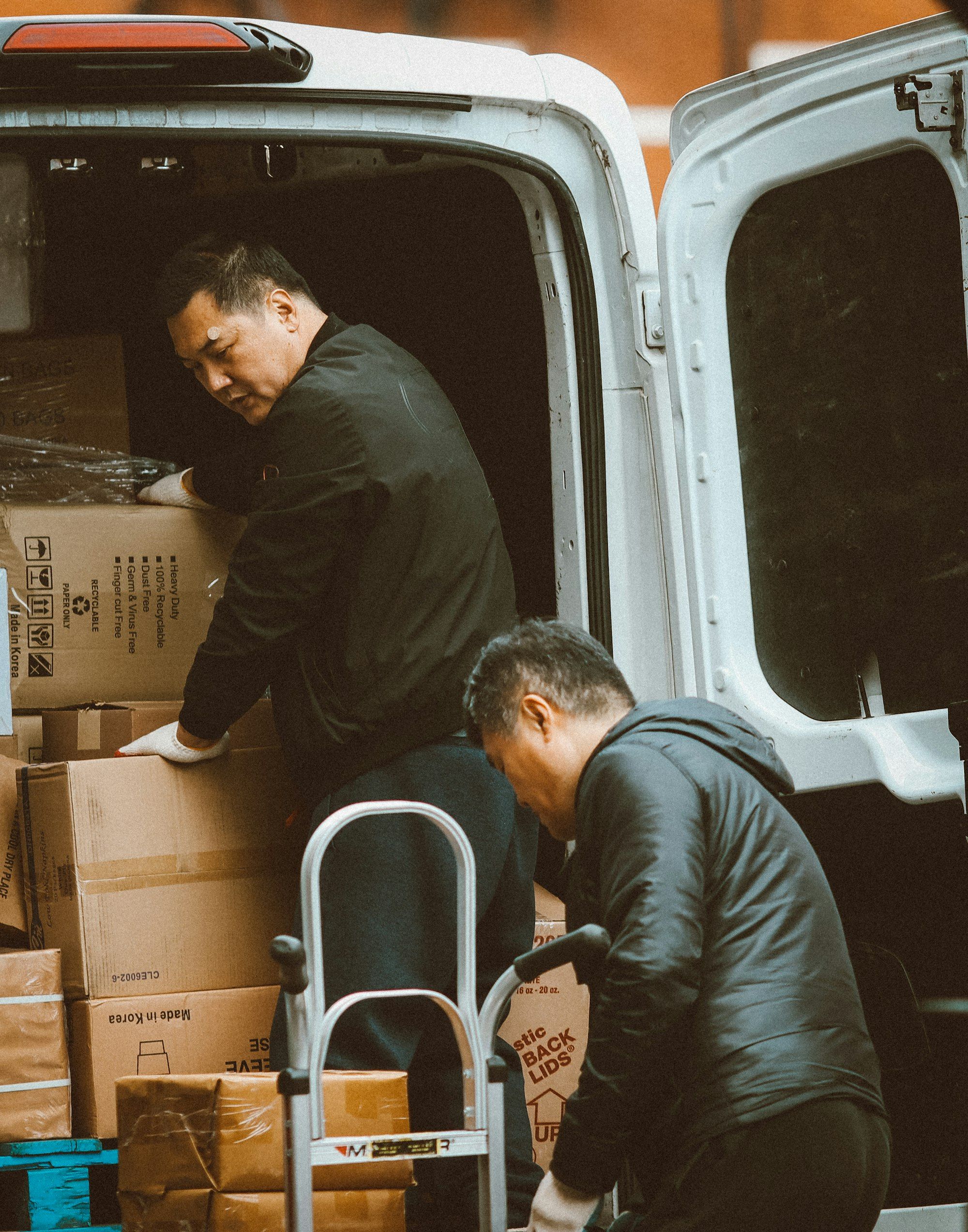 Dos operarios cargando cajas con una carretilla en la parte trasera de una furgoneta